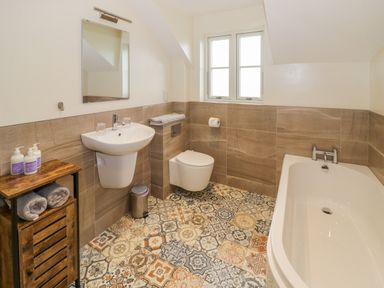 A bathroom with a sink mirror toilet and bathtub with patterned floor tiles at Lavender Cottage in Oxhill near Tysoe