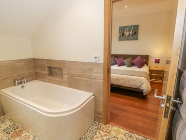 A bathroom with a bathtub and a view into a bedroom with a bed and bedside table at Lavender Cottage in Oxhill near Tysoe