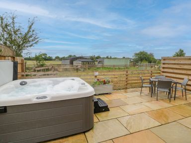 An outdoor patio with a hot tub a table with four chairs and a wooden fence overlooking fields at Lavender Cottage in Oxhill near Tysoe