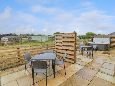 An outdoor patio with two tables and chairs a wooden fence and a hot tub at Lavender Cottage in Oxhill near Tysoe
