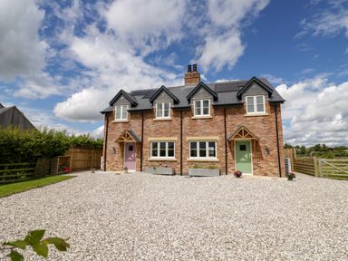 A double fronted brick house with two coloured doors and four windows under a partly cloudy sky at Lavender Cottage in Oxhill near Tysoe