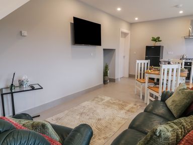 A living room with a mounted television a glass side table green leather sofas with cushions a dining table with white chairs and a black refrigerator in ARD NA GHAOITHE Loughanure County Donegal
