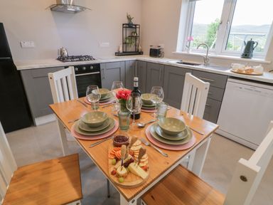 A kitchen with a wooden dining table set for four with plates glasses a cheese platter and a bottle of wine at ARD NA GHAOITHE in Loughanure County Donegal