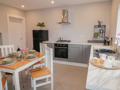 A kitchen with a wooden dining table set with plates and glasses next to grey cabinets and a black refrigerator at ARD NA GHAOITHE in Loughanure County Donegal