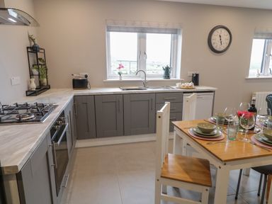 A kitchen with grey cabinets a gas stove and an oven a dining table set with dishes and glasses at ARD NA GHAOITHE in Loughanure County Donegal