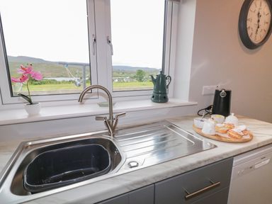 A kitchen sink with a faucet and a window above showing a landscape with hills and houses at ARD NA GHAOITHE in Loughanure County Donegal