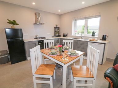 A kitchen with a dining table set for four near a window with gray cabinets and a black refrigerator at ARD NA GHAOITHE in Loughanure County Donegal