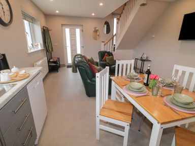A dining area with a wooden table set with plates glasses and a bottle of wine next to a living area with two leather chairs under a staircase