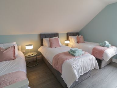 A bedroom with three single beds with pink pillows and throws and bedside tables with lamps at ARD NA GHAOITHE in Loughanure County Donegal