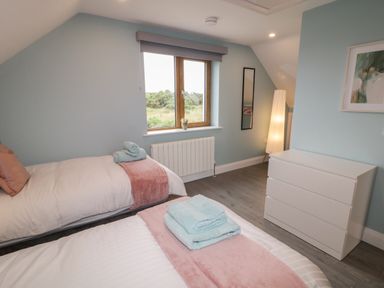 A bedroom with two single beds towels on beds a window a white dresser a floor lamp and a framed picture at ARD NA GHAOITHE in Loughanure County Donegal