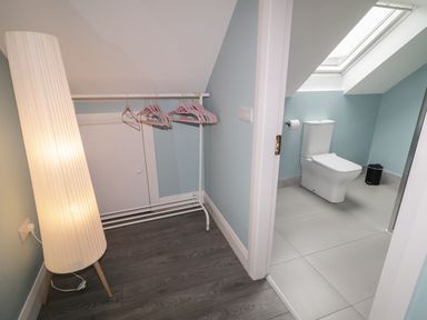 A corner with a standing lamp and a clothes rack with hangers next to a bathroom with a toilet and a skylight at ARD NA GHAOITHE in Loughanure County Donegal