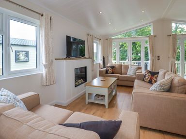 A living room with three beige sofas a wooden coffee table and a wall mounted TV at 43 The Maples in Sticker