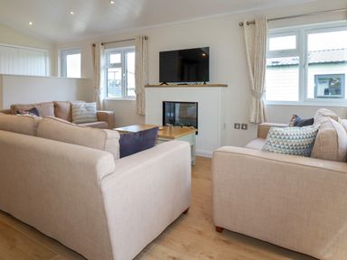 A living room with beige sofas a coffee table a wall-mounted TV and windows with curtains at 43 The Maples in Sticker