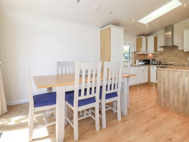 A kitchen and dining area with wooden table and white chairs with blue cushions at 43 The Maples in Sticker