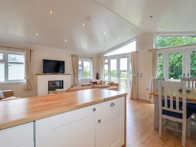 An open-plan living and dining area with a kitchen island a television and sofas at 43 The Maples in Sticker