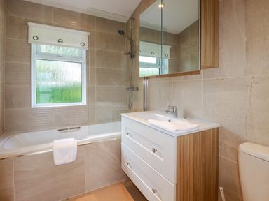 A bathroom with a bathtub shower combination a white vanity with a sink and a large mirror above 43 The Maples Sticker