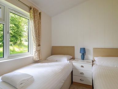 A bedroom with two single beds and a blue lamp on a white bedside table at 43 The Maples in Sticker