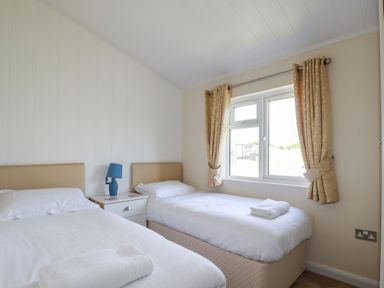 A bedroom with twin beds a bedside table with a lamp and a window with curtains at 43 The Maples in Sticker