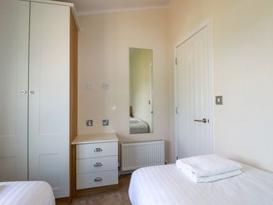 A bedroom with a wardrobe, chest of drawers, wall mirror, radiator, and bed with folded towels at 43 The Maples in Sticker