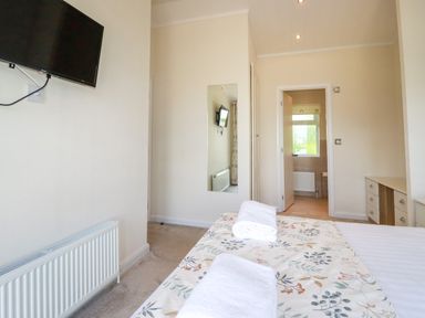 A bedroom with a bed with towels on it a wall-mounted television and an open door leading to a bathroom at 43 The Maples in Sticker