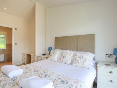 A bedroom with a large bed with floral pillows and a beige headboard with bedside tables and lamps at 43 The Maples in Sticker