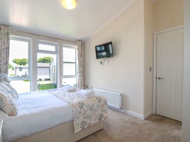 A bedroom with a double bed beside large windows a wall mounted television a radiator and a door at 43 The Maples in Sticker