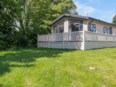 A cabin with a fenced porch surrounded by grass and trees at 43 The Maples in Sticker