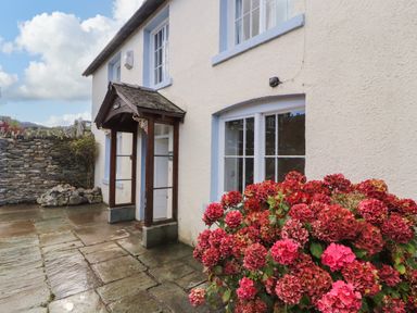 An exterior view of a house with a stone patio and red hydrangea flowers outside Holborn Cottage Blencathra Street Keswick