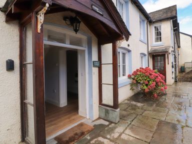 The entrance of a cottage with a wooden doorframe and a doormat outside next to a flower bush at Holborn Cottage Blencathra Street Keswick