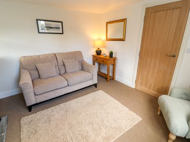 A living room with a beige sofa a wooden side table with a lamp a mirror on the wall and a wooden door at Holborn Cottage Blencathra Street in Keswick