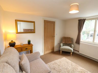 A living room with a sofa and chair next to a wooden door and window at Holborn Cottage Blencathra Street Keswick