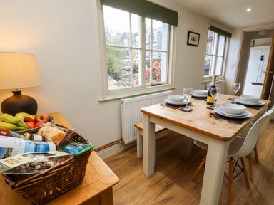 A dining area with a wooden table set for four and a basket of fruit on a side table at Holborn Cottage Blencathra Street in Keswick