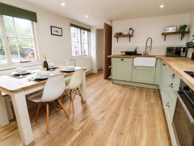 A kitchen with wooden floor green cabinets a dining table with white chairs and tableware at Holborn Cottage Blencathra Street Keswick