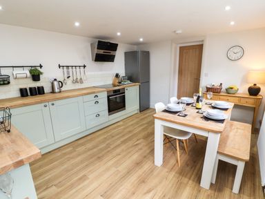 A kitchen with light green cabinets wooden countertops a refrigerator and a dining table set for four at Holborn Cottage Blencathra Street Keswick