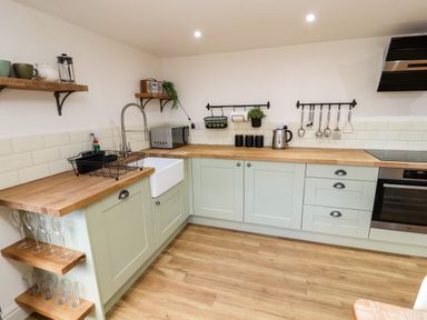 A kitchen with green cabinets wooden countertops a white farmhouse sink and shelves with cups and glasses at Holborn Cottage Blencathra Street Keswick