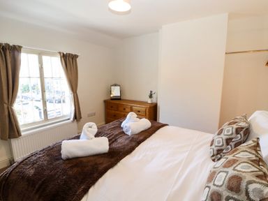 A bedroom with a bed pillows and folded towels on a brown blanket a wooden dresser and window with curtains at Holborn Cottage Blencathra Street in Keswick