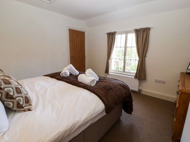 A bedroom with a bed with towels on it a window with curtains and a wooden chest of drawers at Holborn Cottage Blencathra Street Keswick
