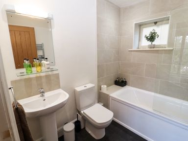 A bathroom with a sink, mirror, toilet, bathtub, and a small window with a plant on the sill at Holborn Cottage, Blencathra Street in Keswick