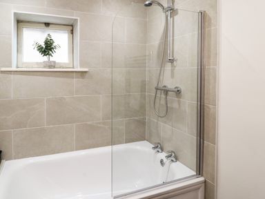 A bathroom with a bathtub shower combination and a small window with a plant on the sill at Holborn Cottage Blencathra Street Keswick