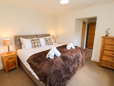 A bedroom with a large bed with brown throw and rolled towels wooden bedside tables and a chest of drawers at Holborn Cottage Blencathra Street Keswick