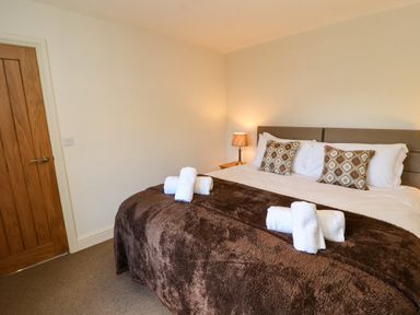 A bedroom with a double bed with white sheets brown blanket and patterned pillows next to a wooden door and a lit table lamp on a bedside table at Holborn Cottage Blencathra Street Keswick
