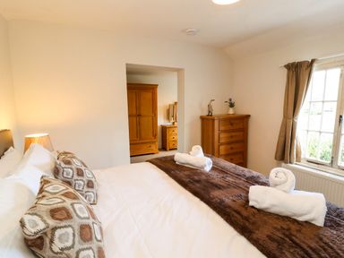 A bedroom with a bed pillows bedside lamp wooden dresser and wardrobe at Holborn Cottage Blencathra Street Keswick
