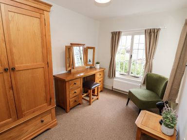 A bedroom with wooden wardrobe dressing table green chair and window at Holborn Cottage Blencathra Street Keswick