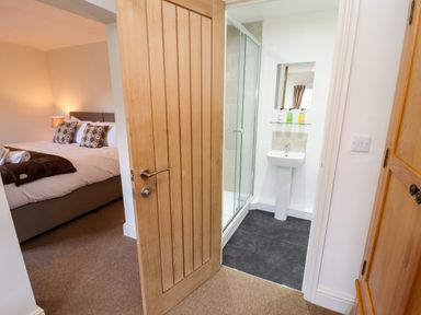 A bedroom with a double bed and a bedside lamp next to a bathroom with a shower and a sink at Holborn Cottage Blencathra Street Keswick