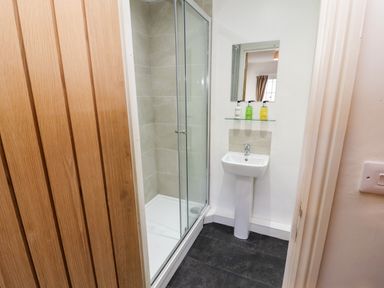 A small bathroom with a shower cubicle a pedestal sink three soap dispensers and a mirror at Holborn Cottage Blencathra Street Keswick