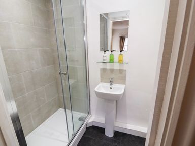A bathroom with a glass door shower enclosure and a pedestal sink with mirror and soap dispensers at Holborn Cottage Blencathra Street Keswick