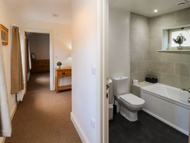 A hallway with a wooden table and a plant next to a bathroom with a toilet and a bathtub at Holborn Cottage Blencathra Street Keswick