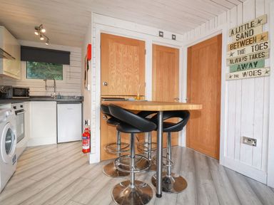 A kitchen with a wooden dining table and black stools and a washing machine next to a window at Villa 18 Lanteglos Holiday Park near Camelford