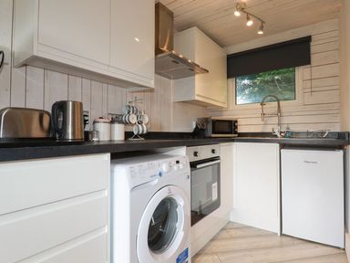 A kitchen with white cabinets a washing machine an oven a fridge a microwave a toaster and a kettle at Villa 18 Lanteglos Holiday Park near Camelford