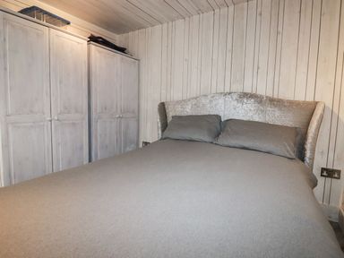 A bedroom with a double bed and a wardrobe against wooden paneled walls at Villa 18 Lanteglos Holiday Park near Camelford